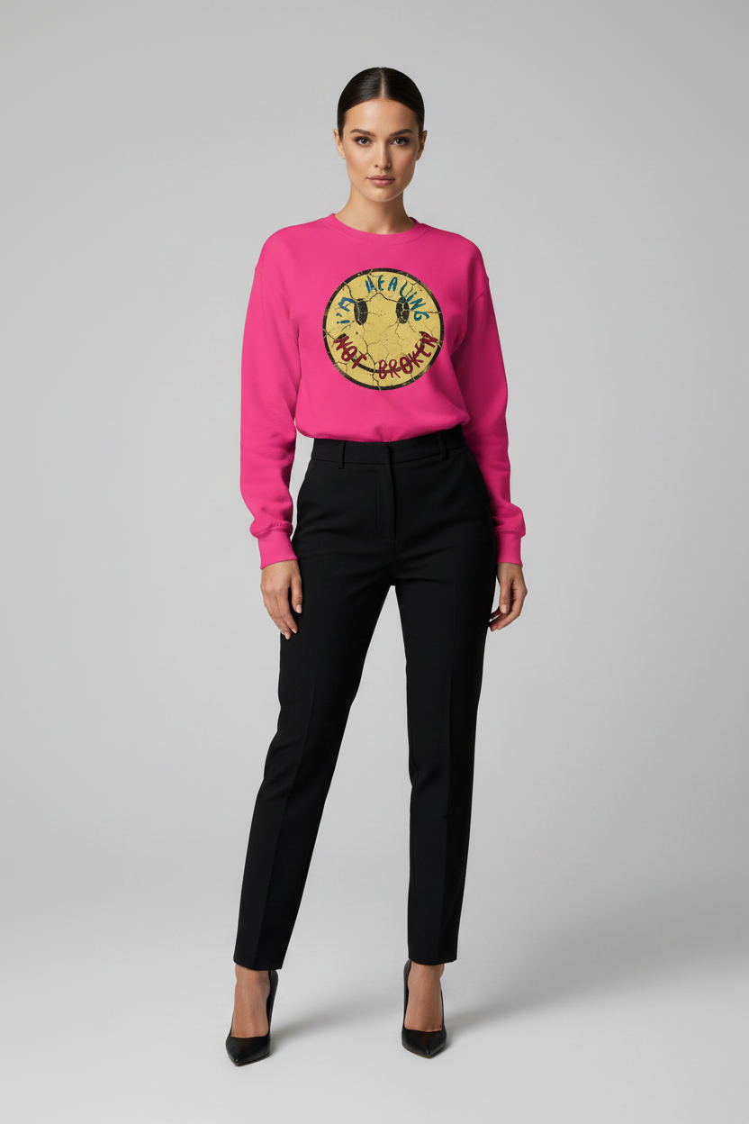 Woman wearing a pink sweater with a colorful logo and black pants on a gray background