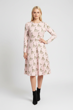 A woman modeling a light pink long-sleeve midi dress with an allover sailboat print, paired with black ankle boots, against a light gray studio background.