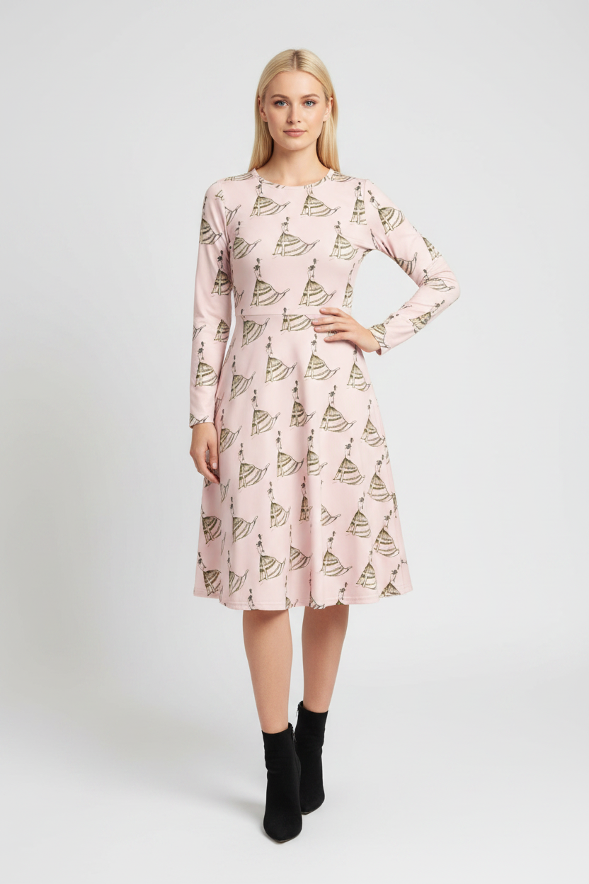 A woman modeling a light pink long-sleeve midi dress with an allover sailboat print, paired with black ankle boots, against a light gray studio background.