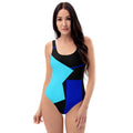 A full-body front view of a model wearing a geometric color block one-piece swimsuit with a bold design.