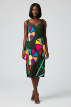 Woman wearing a green dress with colorful abstract patterns on a white background. Woman modelling an APPARELHUE graphic print slip dress paired with metallic gold heeled sandals.