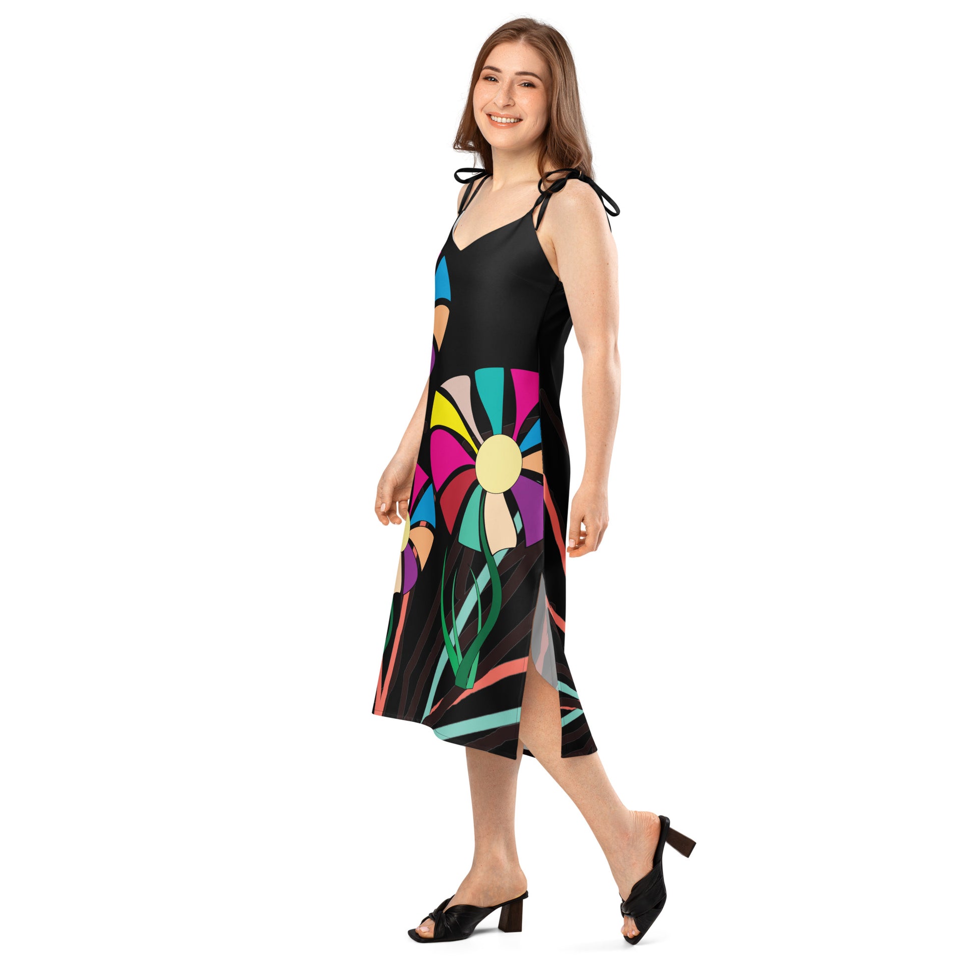 Full-length view of a woman wearing a green midi dress with a colorful abstract floral pattern, featuring tie straps and a high side slit.