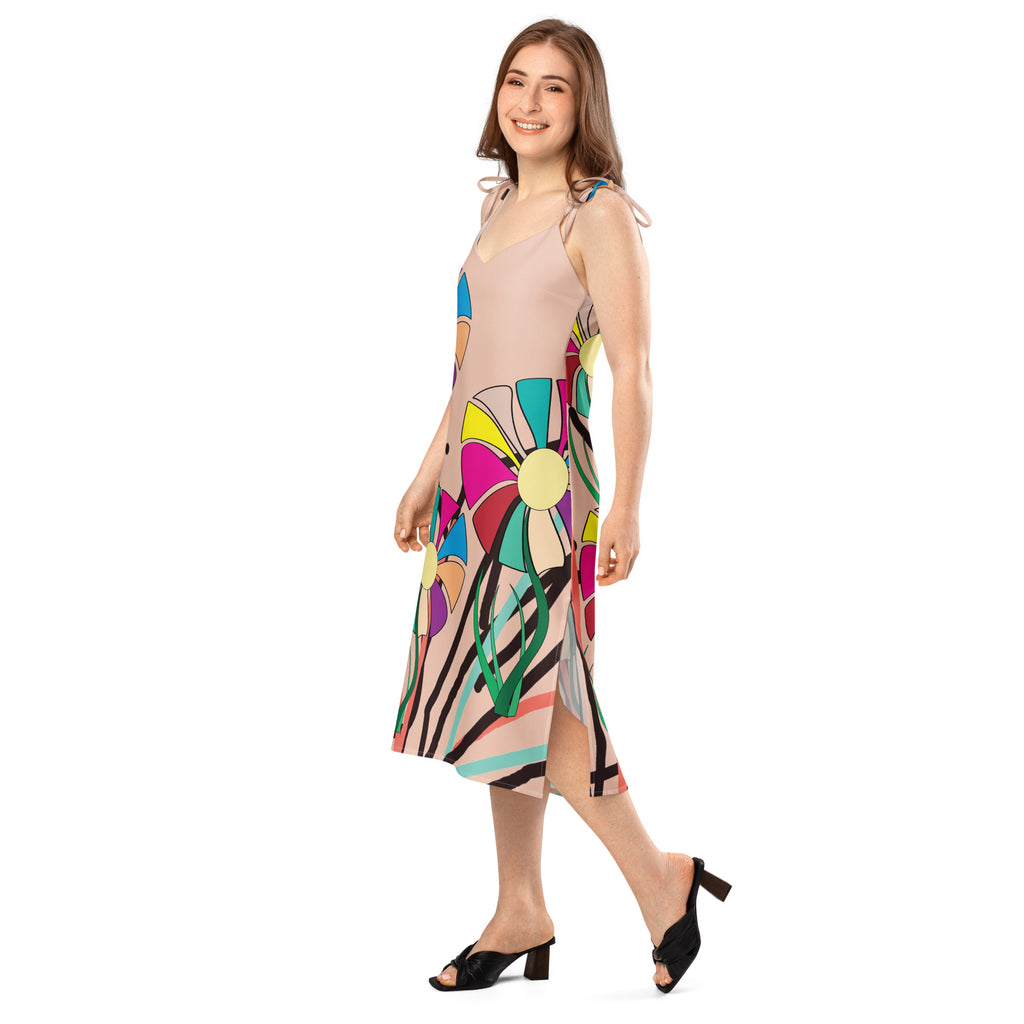 A woman modeling a sleeveless midi dress with a beige base and a colorful retro floral pattern, paired with black mule heels, on a solid white background.