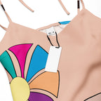 Close-up of one of the abstract flowers on the dress, with its multi-colored petals and yellow center, against the peach background.