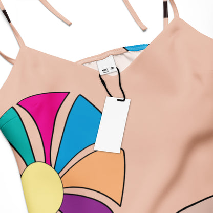 Close-up of one of the abstract flowers on the dress, with its multi-colored petals and yellow center, against the peach background.