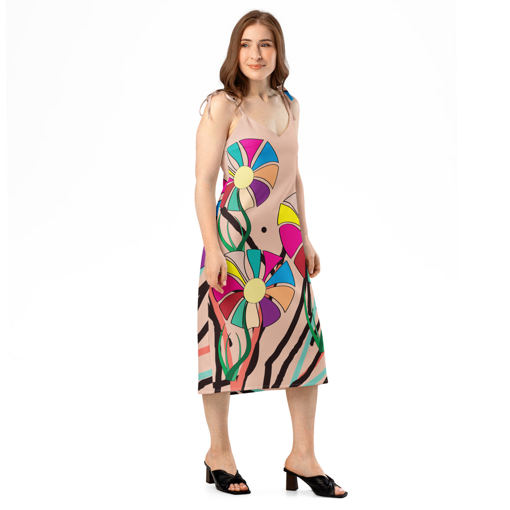 A woman modeling a sleeveless midi dress with a beige base and a large, colorful retro floral and abstract print, paired with black heeled sandals against a plain white background.