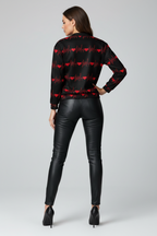 Woman wearing a black shirt with red heart patterns and black leather pants on a gray background