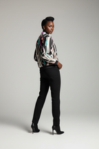 Woman wearing a patterned blouse and black pants on a gray background