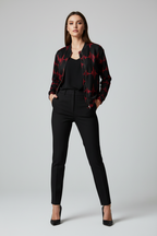 A woman modeling a black satin bomber jacket with a red EKG-style heartbeat pattern, paired with black trousers and heels, against a light gray studio background.