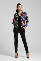 A woman modeling a dark green patterned bomber jacket with pink, blue, and beige abstract stripes, worn over a black top and black pants, against a light gray studio background.
