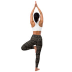 Woman in a Warrior II yoga pose, demonstrating the flexibility and fit of the black and gold patterned yoga leggings.