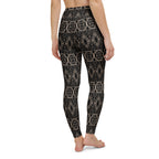 Back view of a woman wearing black leggings with a shimmering gold intricate pattern.