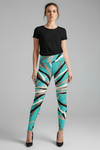 A woman modeling high-waisted leggings with a bold abstract geometric pattern in turquoise, beige, black, and gray, paired with a black t-shirt and black heels, against a neutral gray studio background.