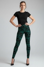 A woman modeling high-waisted black leggings with a vibrant green abstract line pattern, paired with a black short-sleeve t-shirt and black heels, against a light gray studio background.