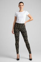 A woman modeling black leggings with a gold chain-link pattern, paired with a white t-shirt and black heels, against a light gray studio background.