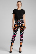 A model wearing high-waisted black leggings with a colorful abstract geometric print, paired with a black t-shirt and black heels, against a neutral gray background.