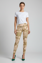 A model stands against a light gray studio background wearing high-waisted leggings with a beige and olive geometric pattern, a white t-shirt, and green high heels.