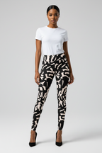 A model stands against a light gray studio background wearing a white short-sleeve crewneck top, black and beige abstract patterned leggings, and black high heels.