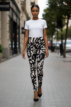 A woman walking down a city street wearing a white short-sleeve crewneck t-shirt and high-waisted black and beige abstract patterned leggings with black pointed-toe heels.