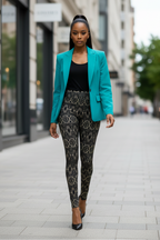 A woman walking down a city street wearing a bright turquoise blazer, a black top, and black leggings with a beige geometric pattern, paired with black pointed-toe heels.