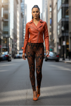 A woman walking down a city street wearing a rust-orange leather moto jacket, brown and black paisley patterned leggings, and matching orange heels.