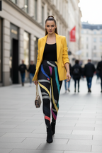 A woman walking down a city street wearing a bright yellow blazer, a black top, and colorful abstract-print leggings, carrying a small handbag.