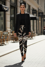 A woman walking on a city street wearing a black blazer, black top, and black leggings with a beige and gray abstract geometric pattern, paired with black pointed-toe heels.