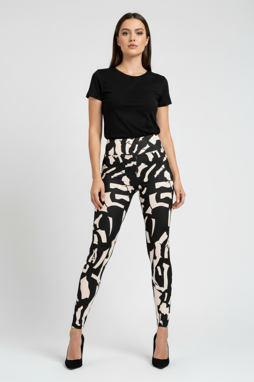 A woman modeling high-waisted leggings with a black and beige abstract brushstroke pattern, paired with a black short-sleeve t-shirt and black heels, against a light gray studio background.