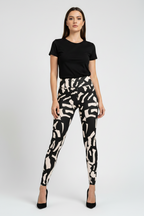 A woman modeling high-waisted leggings with a black and beige abstract brushstroke pattern, paired with a black short-sleeve t-shirt and black heels, against a light gray studio background.
