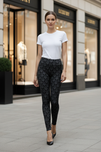 A woman walking on a city sidewalk wearing a white short-sleeve crewneck t-shirt and black patterned leggings with black pointed-toe heels. The background shows storefront windows with the brand name 'L'AMOUR'.
