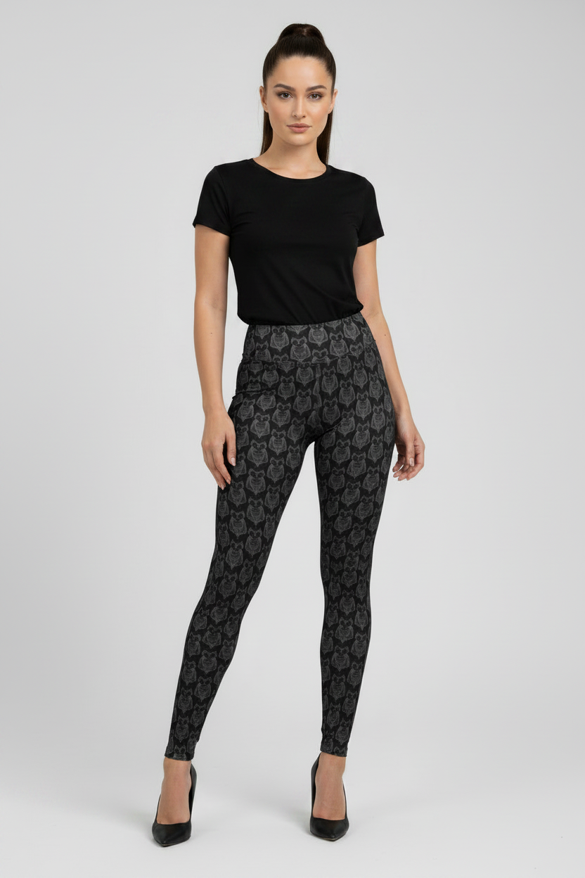 A woman modeling black patterned leggings with a black short-sleeve top and black heels, standing against a light gray studio background.