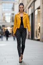 A woman walking down a city street wearing a bright yellow moto jacket over a black top and black patterned leggings.
