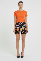 Woman wearing an orange t-shirt and colorful patterned shorts on a white background