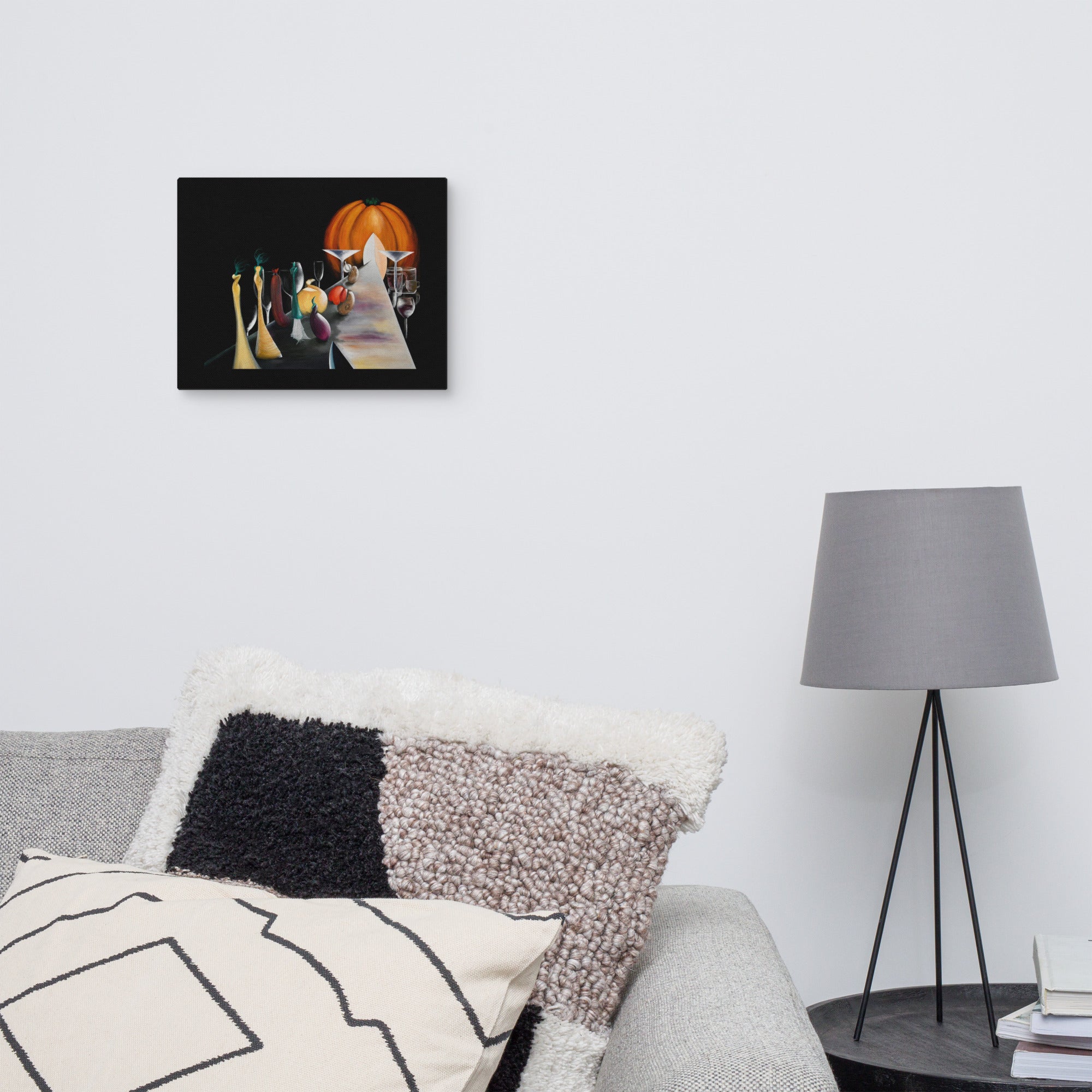 A framed wall art print depicting a stylized Halloween scene with a pumpkin, candles, and a cat, displayed on a light gray wall above a sofa with decorative pillows and a floor lamp.