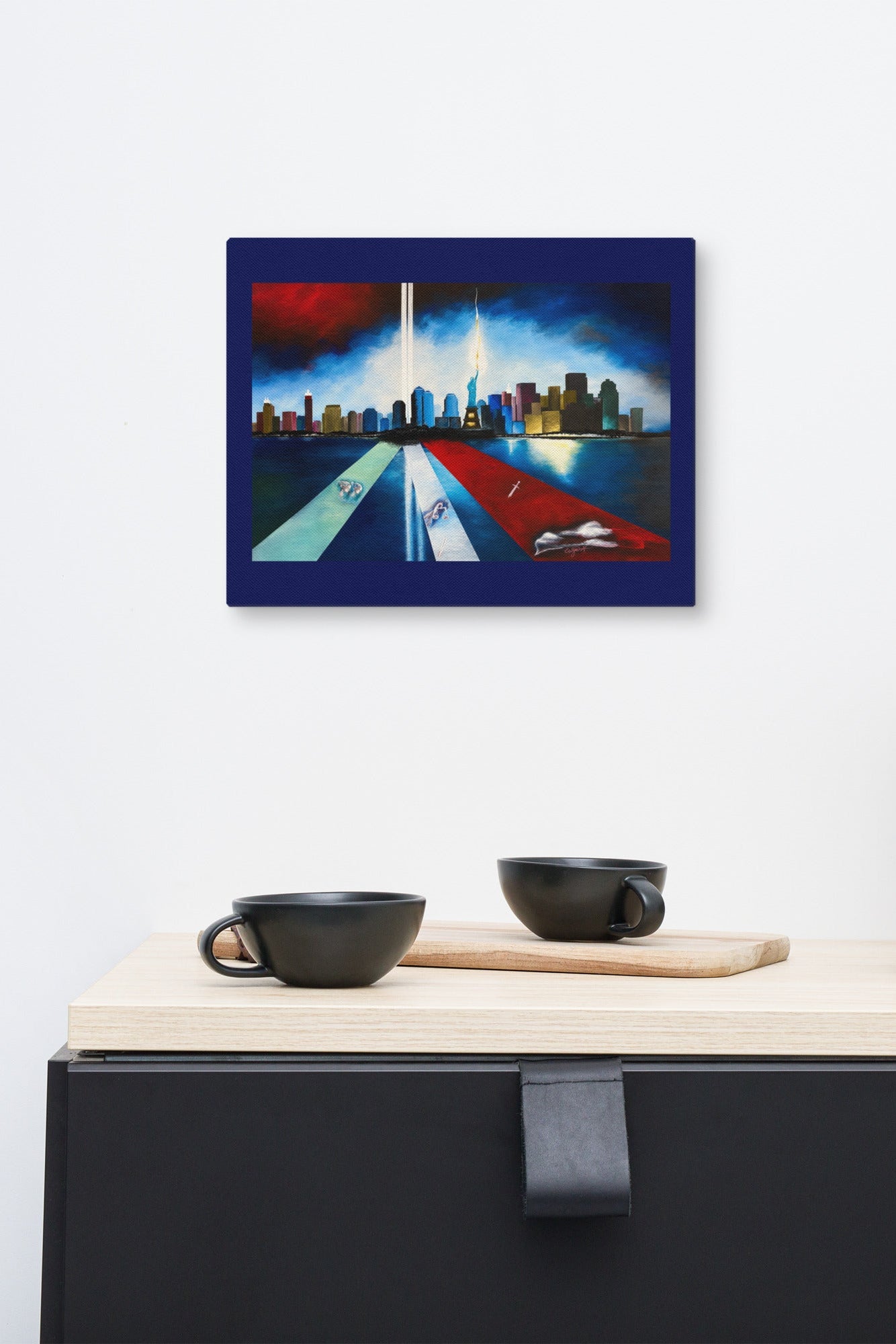A rectangular wall art print showing a stylized city skyline with a bright beam of light, displayed above a kitchen counter with black cups and utensils against a white wall.