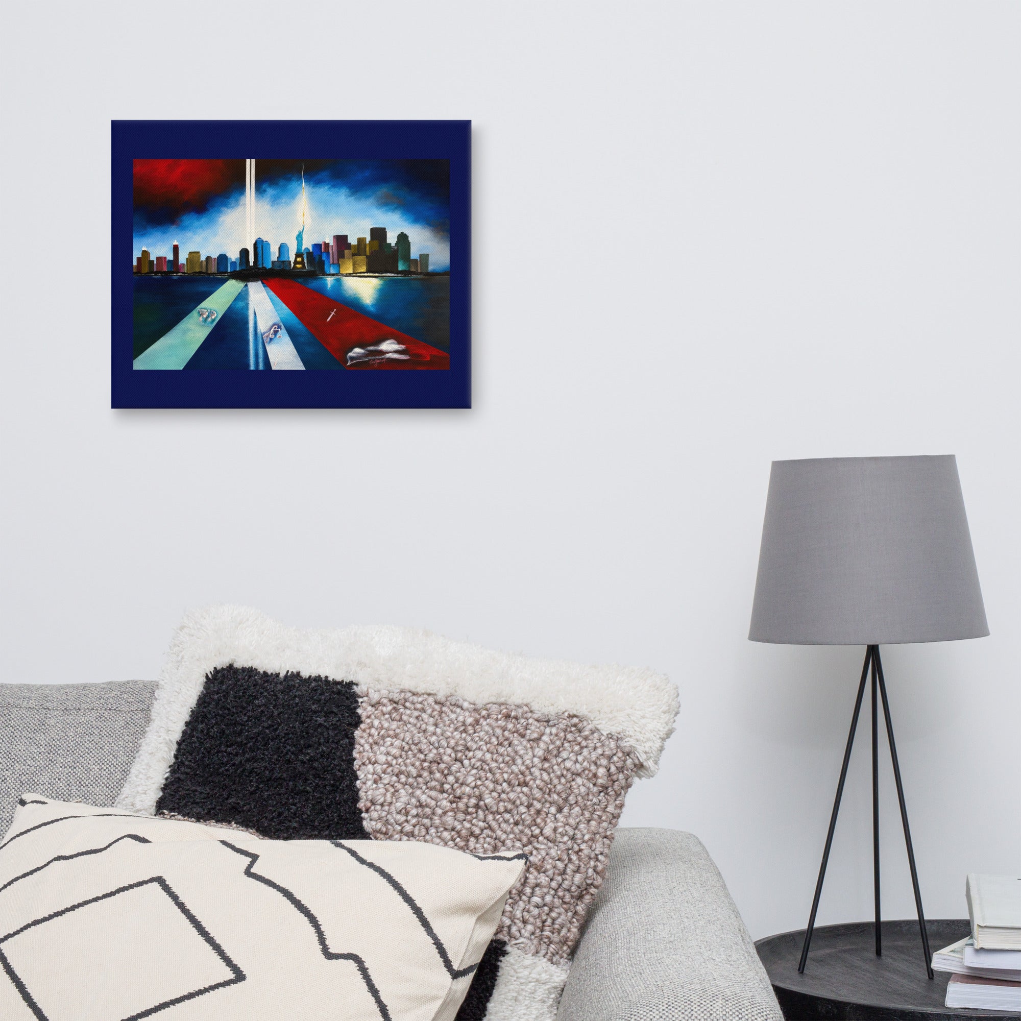 A framed abstract cityscape canvas print with a dark blue border hangs on a light gray wall above a sofa with textured pillows, next to a gray floor lamp.