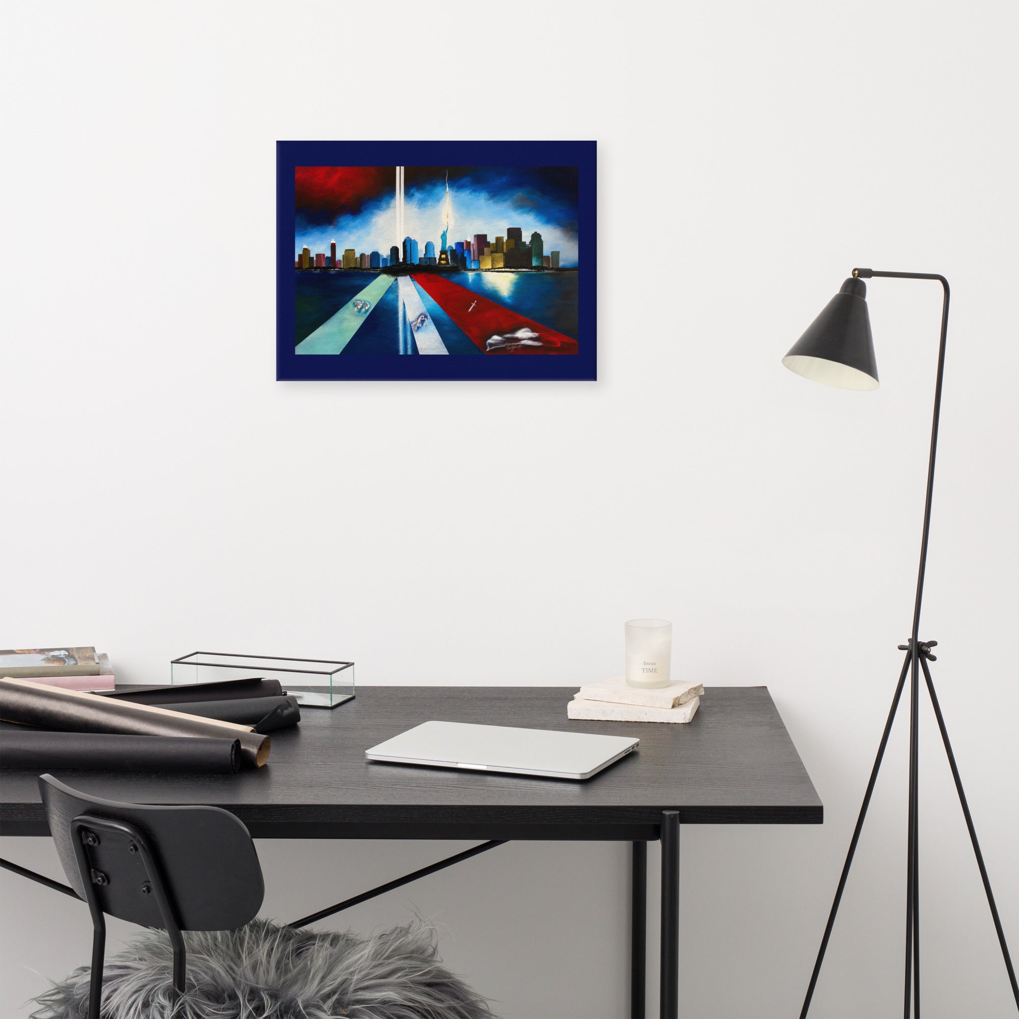 A framed art print depicting the Twin Towers of the World Trade Center with red and white light beams, displayed on a white wall above a modern black desk setup with a chair and floor lamp.