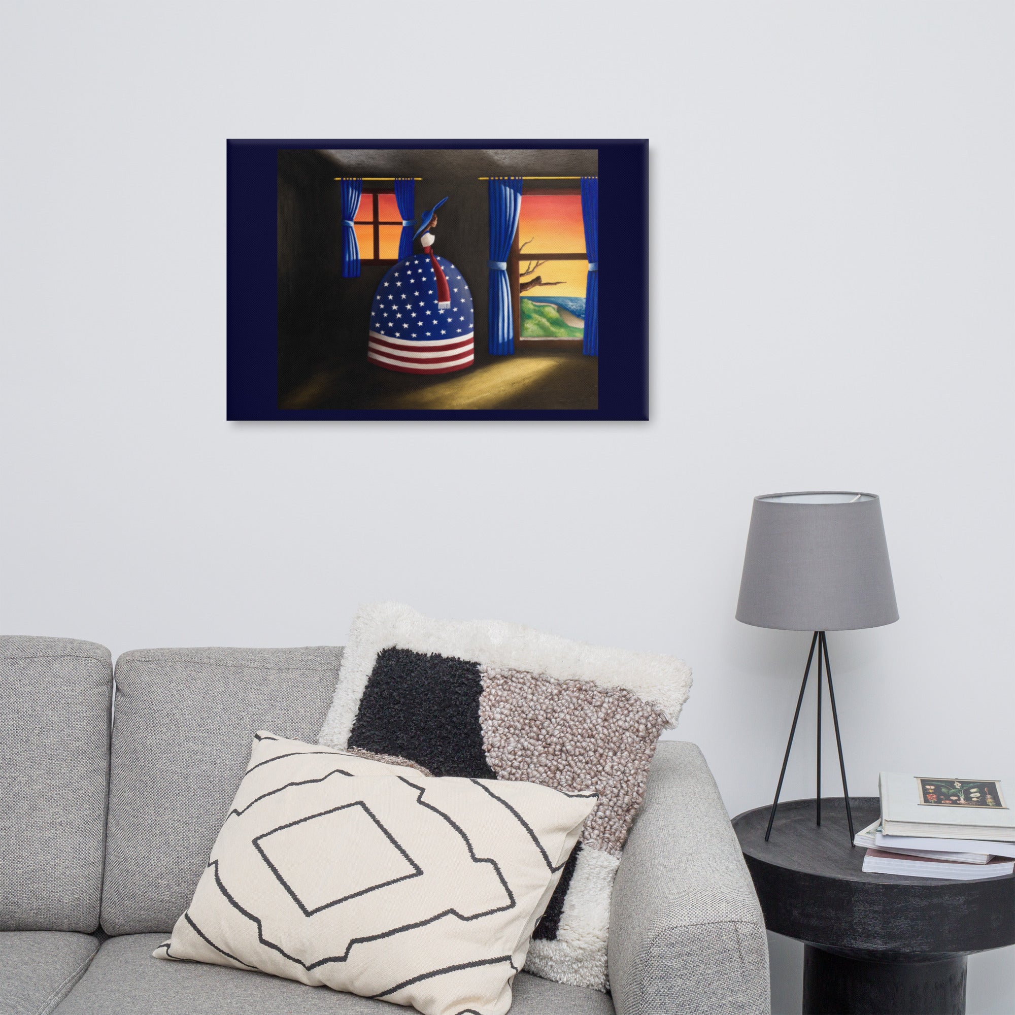 A framed wall art print depicting a stylized figure in an American flag-patterned dress standing in a doorway at sunset, displayed above a gray sofa with decorative pillows in a living room setting.