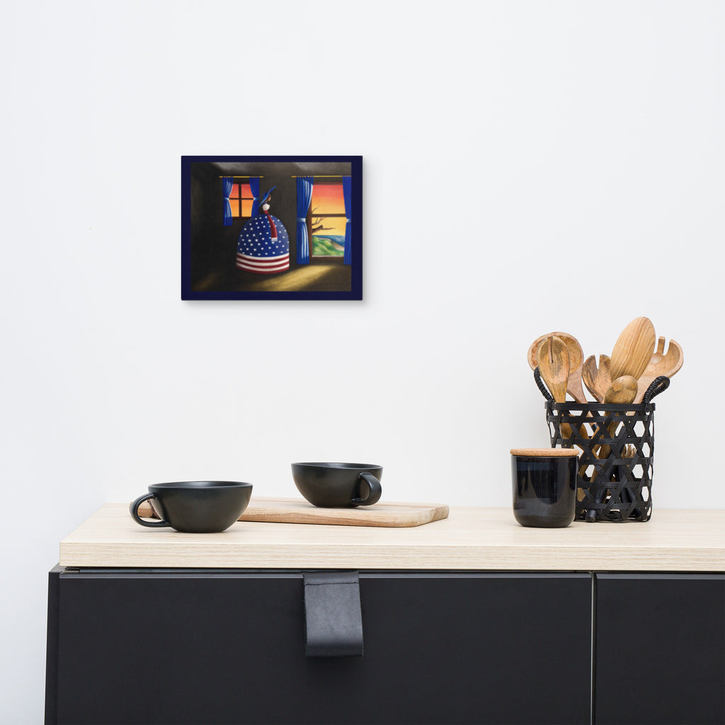 A framed wall art print depicting a colorful still life with an American flag patterned pot and warm glowing windows, displayed on a white wall above a kitchen counter with black mugs and utensils.