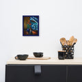 A small framed art print depicting a shark in a kitchen scene hangs on a white wall above a light wood counter with black mugs and a utensil holder.