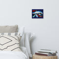 A small square wall art print depicting a stylized city skyline with red, white, and blue tones, displayed above a bed in a minimalist bedroom setting.