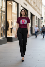 A woman walking down a city street wearing a maroon short-sleeve t-shirt with a graphic print of red lips on a gray background, paired with black trousers and black heels.