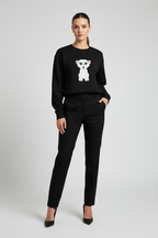 Woman wearing a black sweater with a white bear design and black pants on a light gray background