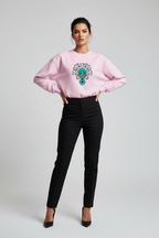 Woman wearing a pink sweatshirt with a colorful design and black pants on a light gray background