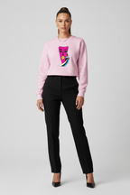 Woman wearing a pink sweater with a colorful design and black pants on a light gray background