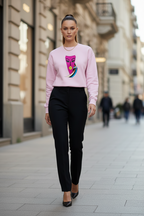 Woman wearing a pink sweater with a graphic design on a city street.