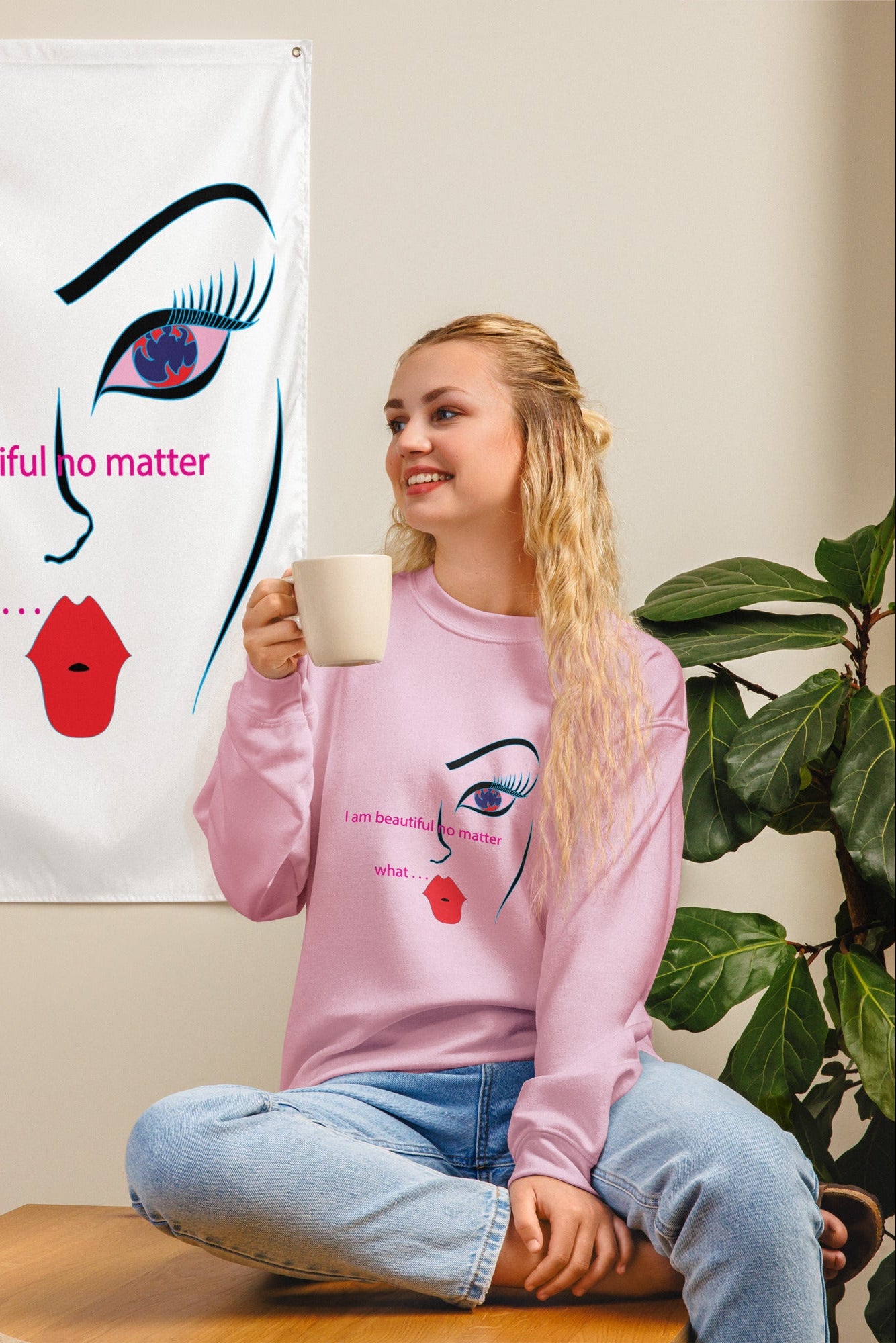 A woman sitting and smiling, holding a coffee cup, with a graphic sweatshirt featuring an abstract art design and the text 'I am beautiful, ho matter what.