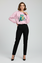 Woman wearing a pink sweatshirt with an owl design and black pants on a white background