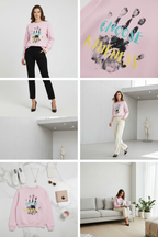A female model standing against a plain white studio background wearing the APPARELHUE light pink unisex crew-neck sweatshirt featuring a "CHOOSE KINDNESS" graphic text overlay on a black handprint, paired with tailored black trousers.