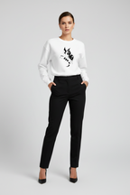Woman wearing a white sweater with black design and black pants on a light gray background